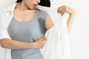 Close up of a woman looking at the sweat stains on her shirt in shock, in need of treatment.